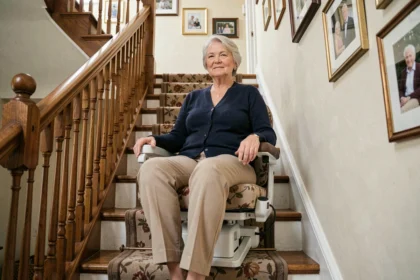 Femme âgée assise sur un monte-escalier portable installé sur un escalier en bois dans une maison traditionnelle